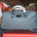 gray and black checkerboard pattern travel holdall bag featuring dark leather trim and a central logo plaque.