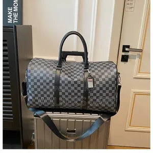 gray and black checkerboard pattern travel holdall bag featuring dark leather trim and a central logo plaque.